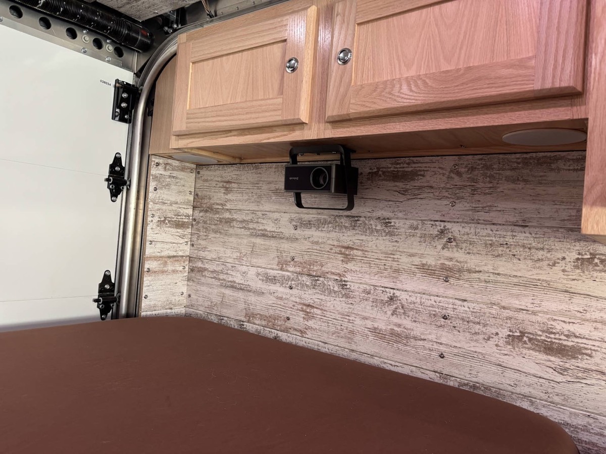 Finished overhead oak cabinets above a shiplap-panelled van wall and bed