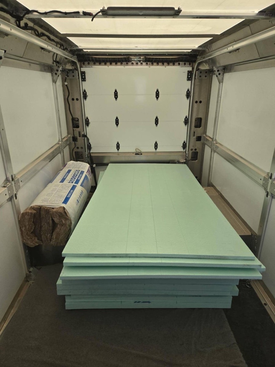 Stack of rigid XPS foam sheets and a fiberglass bundle inside a bare van